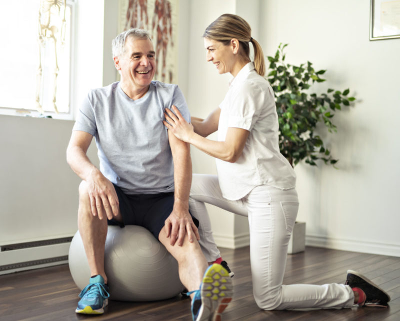 rehabilitation physiotherapy worker with senior client sitting on a gym ball