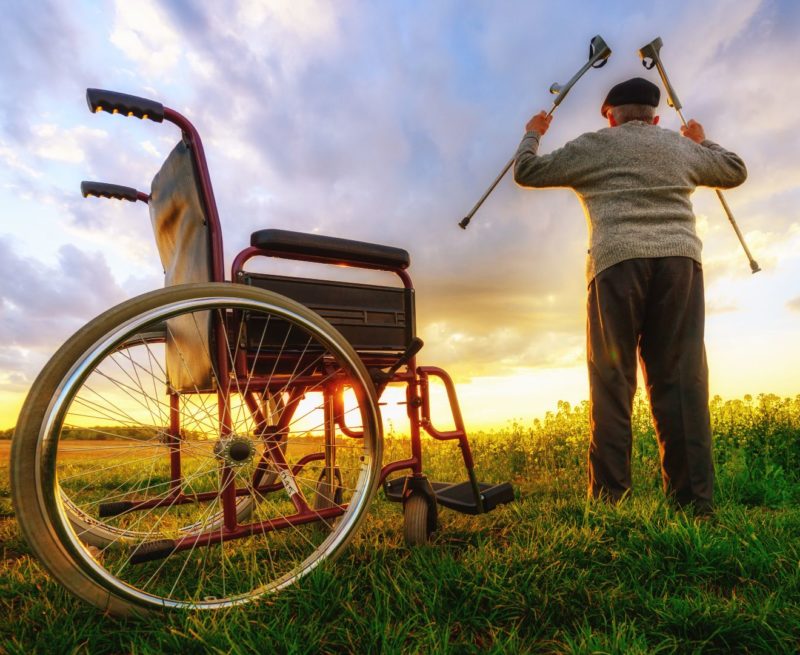 man standing by his wheelchair holding his elbow crutches high in the air